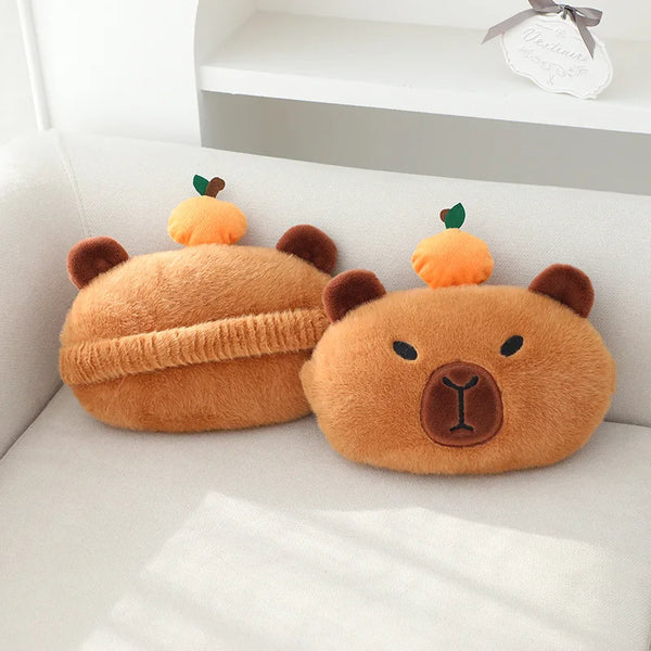 A fluffy orange plush capybara shaped like a bear is resting on a white sofa cushion.