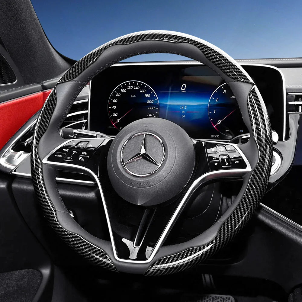 Close-up of a black steering wheel with carbon fiber texture cover inside a modern car interior.
