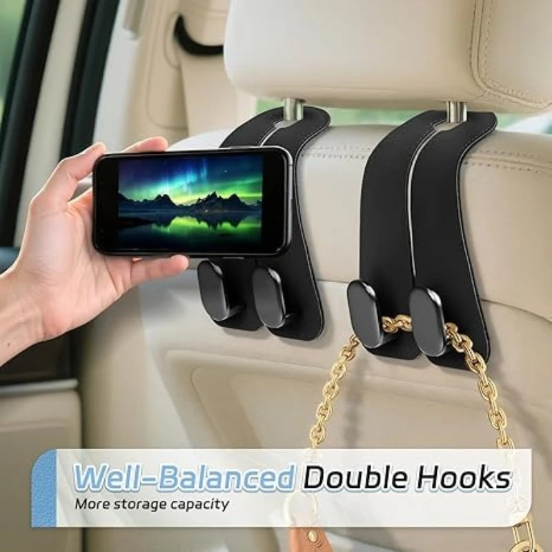A hand holds a smartphone attached to black double hooks mounted on a car headrest for storage organization.
