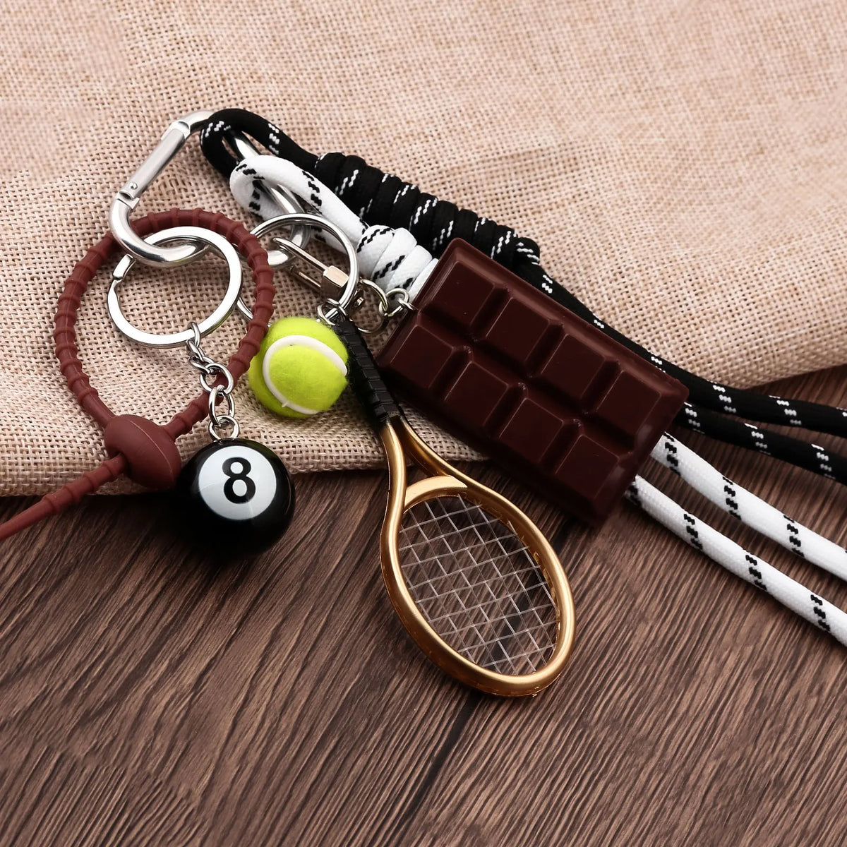A sporty billiard bag charm keychain featuring a wooden paddle, a tennis ball, and a chocolate bar attached to leather and co