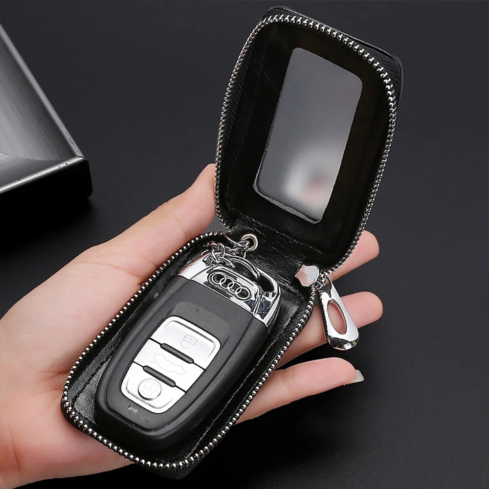 A hand holds an open black leather car key protector pouch with a silver key inside.