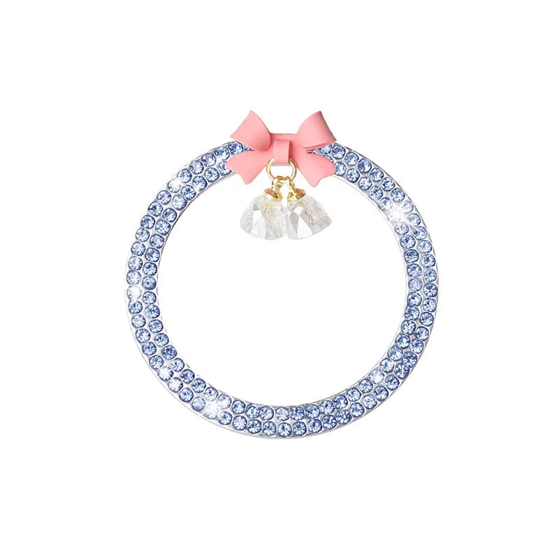 A round rhinestone trim featuring blue stones and a pink bow with a dangling bell.