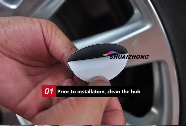 A hand holds a black and white car wheel hub center cap decal for installation.