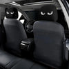 Two black car headrest covers with funny slanted eyes are shown inside a vehicle cabin.