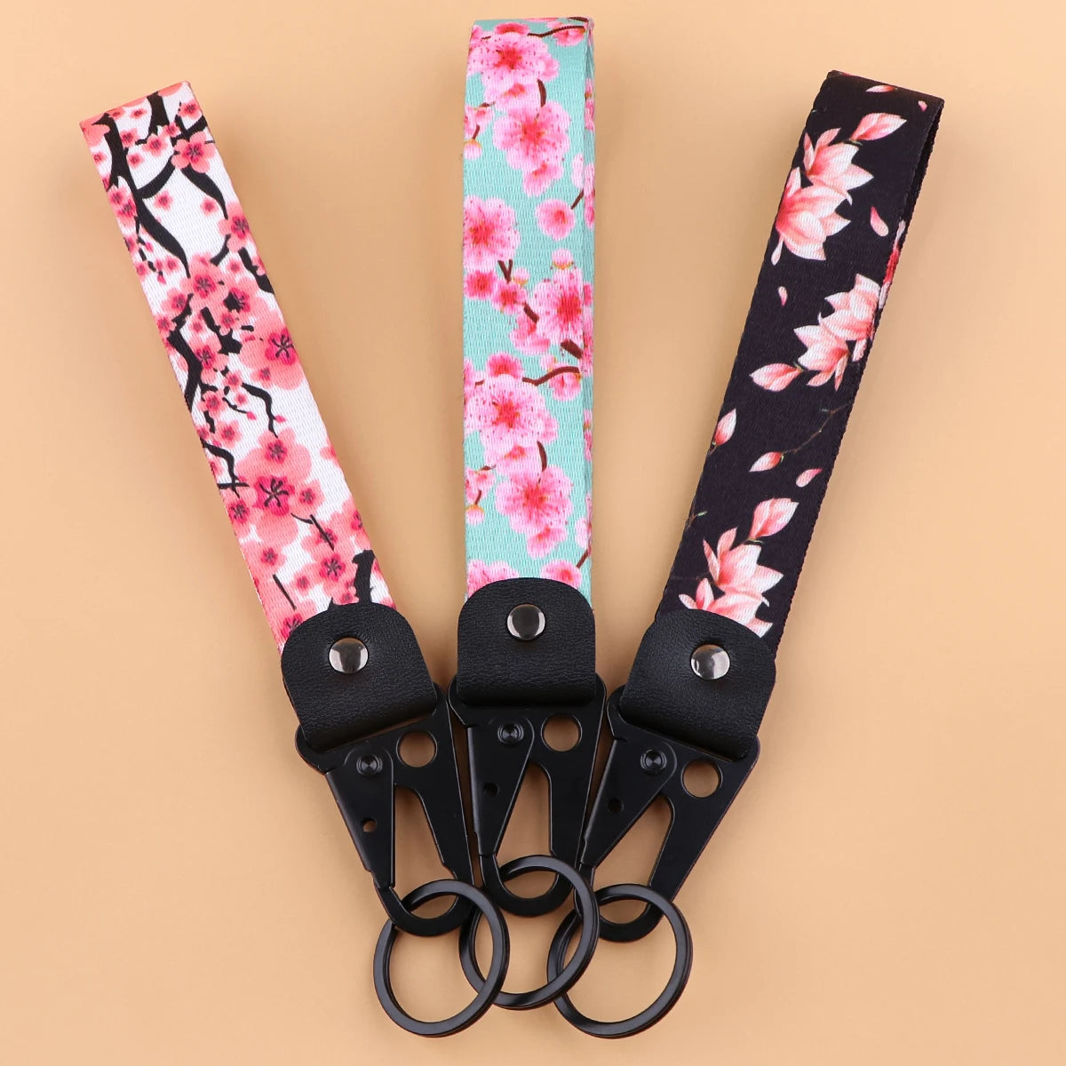 A set of three pink and black floral patterned wrist straps with metal clasps and split rings.