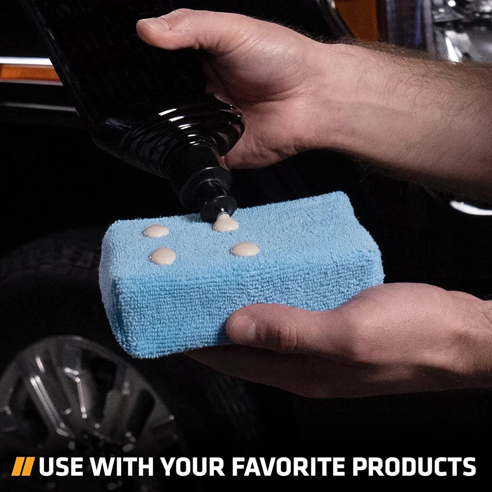 A hand is applying a substance from a bottle onto a blue microfiber polishing pad for car wax application.