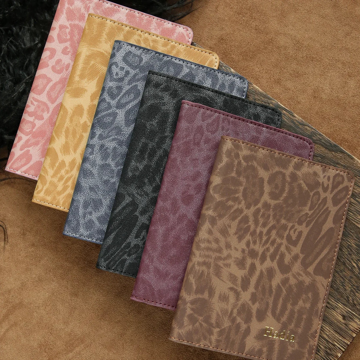 A collection of five leather passport holders in various leopard print patterns and colors stacked on a brown surface.