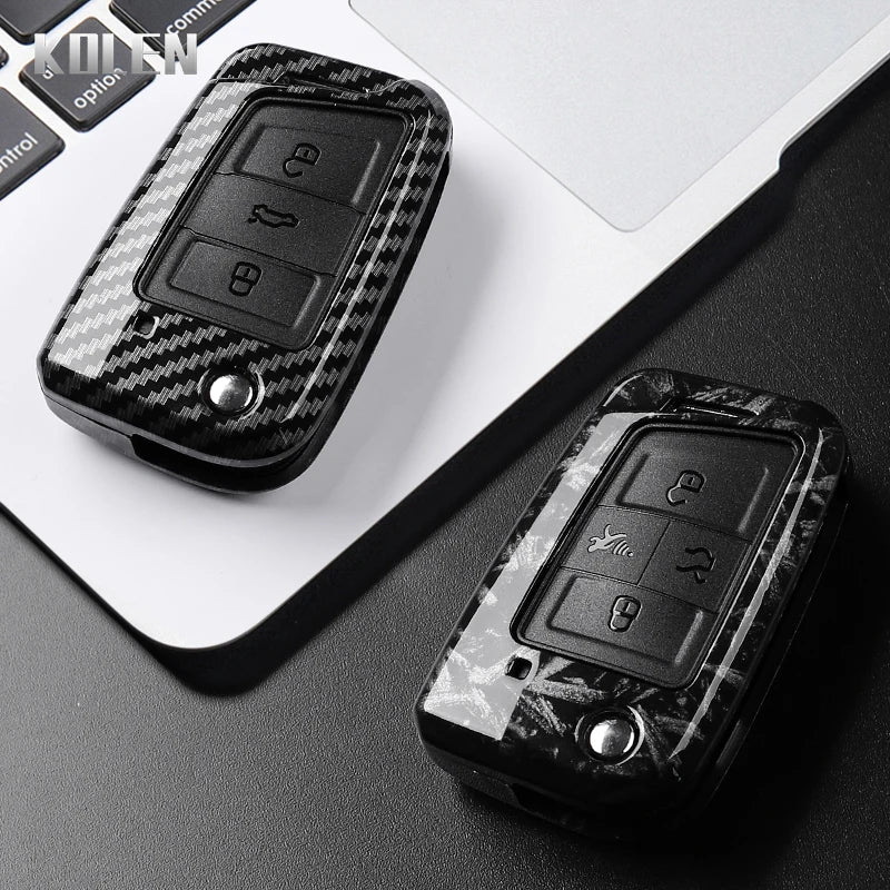 A black carbon fiber button cover for a car key is displayed on a white laptop surface.