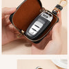 A brown leather pouch with a zipper holds an Audi car key fob and a decorative metal charm.