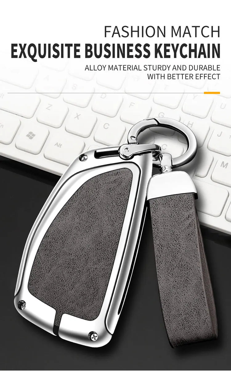 A silver key chain with a textured gray cover and black strap resting on a white computer keyboard.