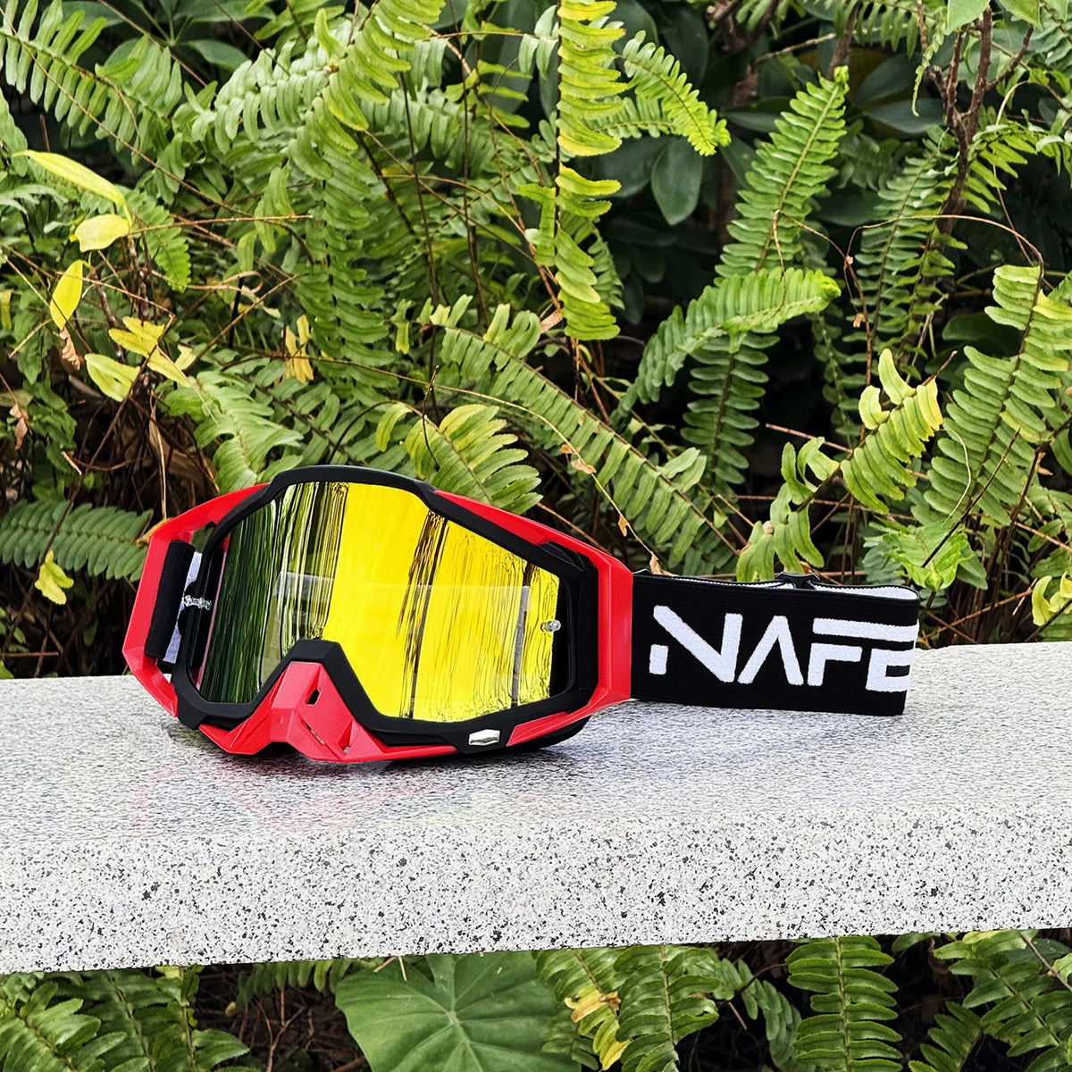 Une paire de lunettes de sport pour moto rouges et noires durables avec des verres teintés jaunes, posées sur une surface gri