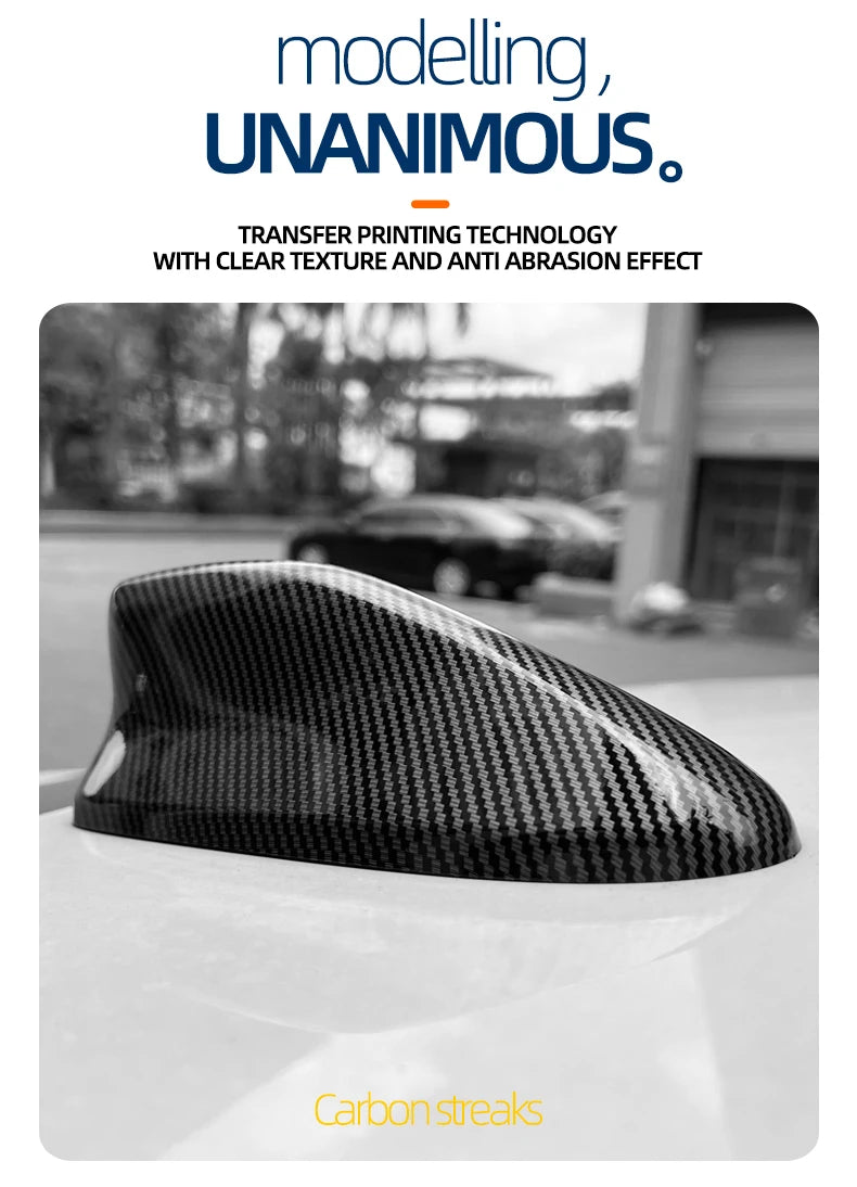 Close-up of a black carbon streak roof antenna cover placed on a white car surface.