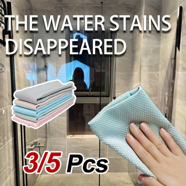 A hand holds a light blue reusable glass cleaning cloth, with a stack of three similar cloths visible in the background.