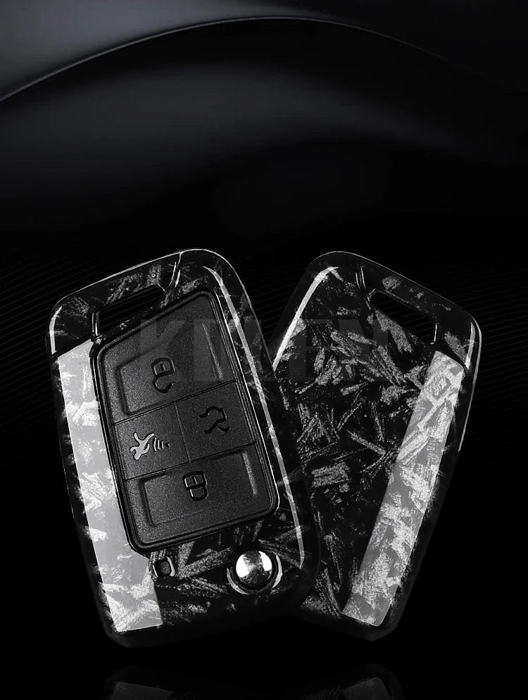 A black carbon fiber button cover for a car key, shown in a close-up against a dark background.