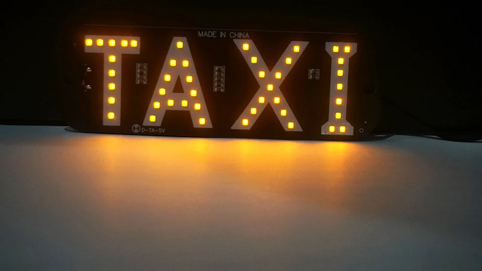 An illuminated sign displaying the word TAXI made in CHINA, featuring bright yellow LED lights.