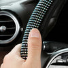 A hand is holding a black steering wheel cover adorned with sparkling crystal diamond rhinestones.