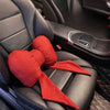Un oreiller de cou en tissu rouge est placé sur l'appui-tête d'un siège de voiture noir.