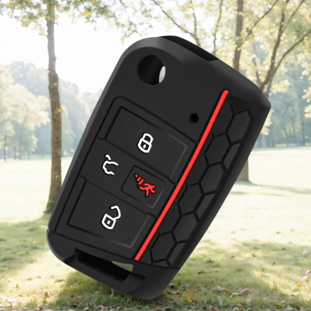 A black silicone car key cover is shown lying on grass with trees in the background.