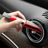 A hand is using a red and silver brush to clean a car air vent grille.