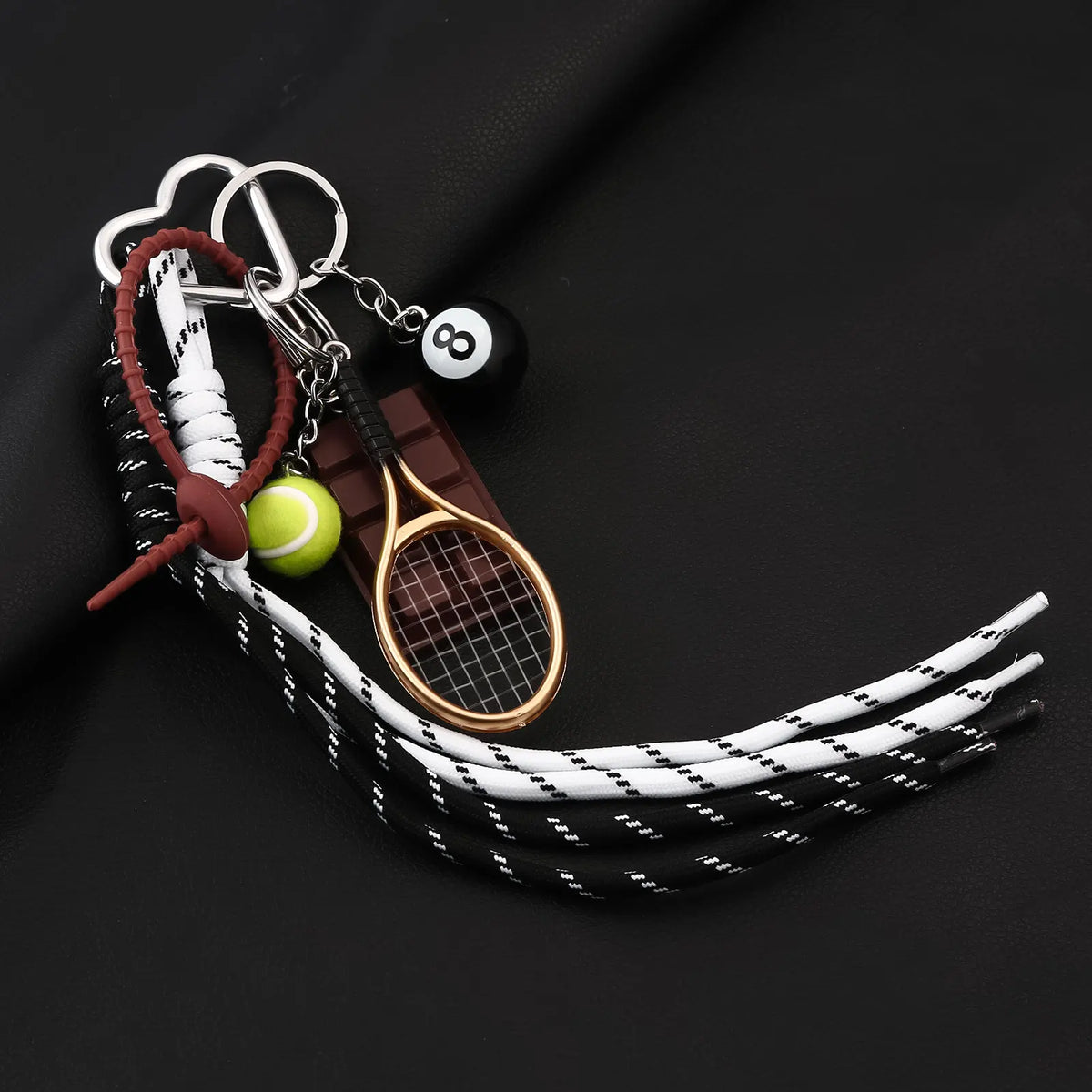 A sporty billiard bag charm keychain featuring a wooden racket, a yellow tennis ball, and black and white striped cord.