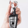 A hand holds a silver and black leather keychain with a split ring and various metal components.