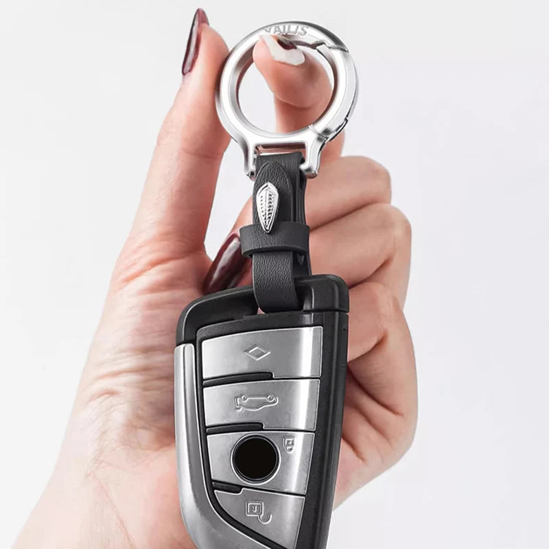 A hand holds a silver and black leather keychain with a split ring and various metal components.