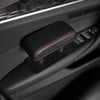 A black ergonomic vehicle armrest cushion with red stitching is shown in a car interior.