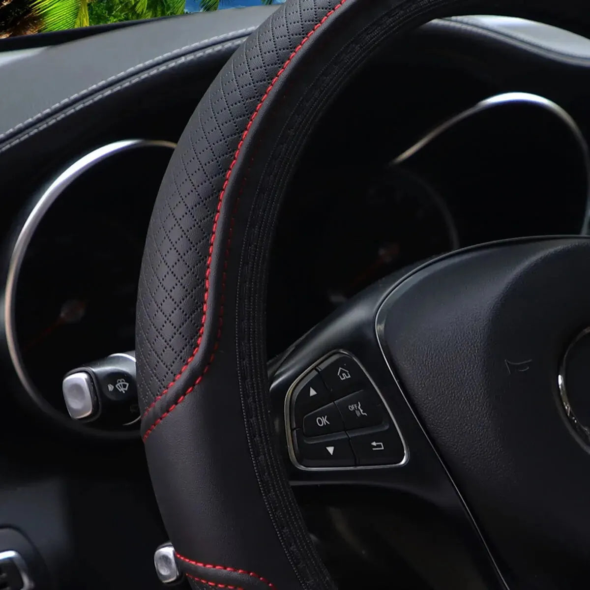 Close-up view of a black embossed leather steering wheel cover with red stitching and controls.