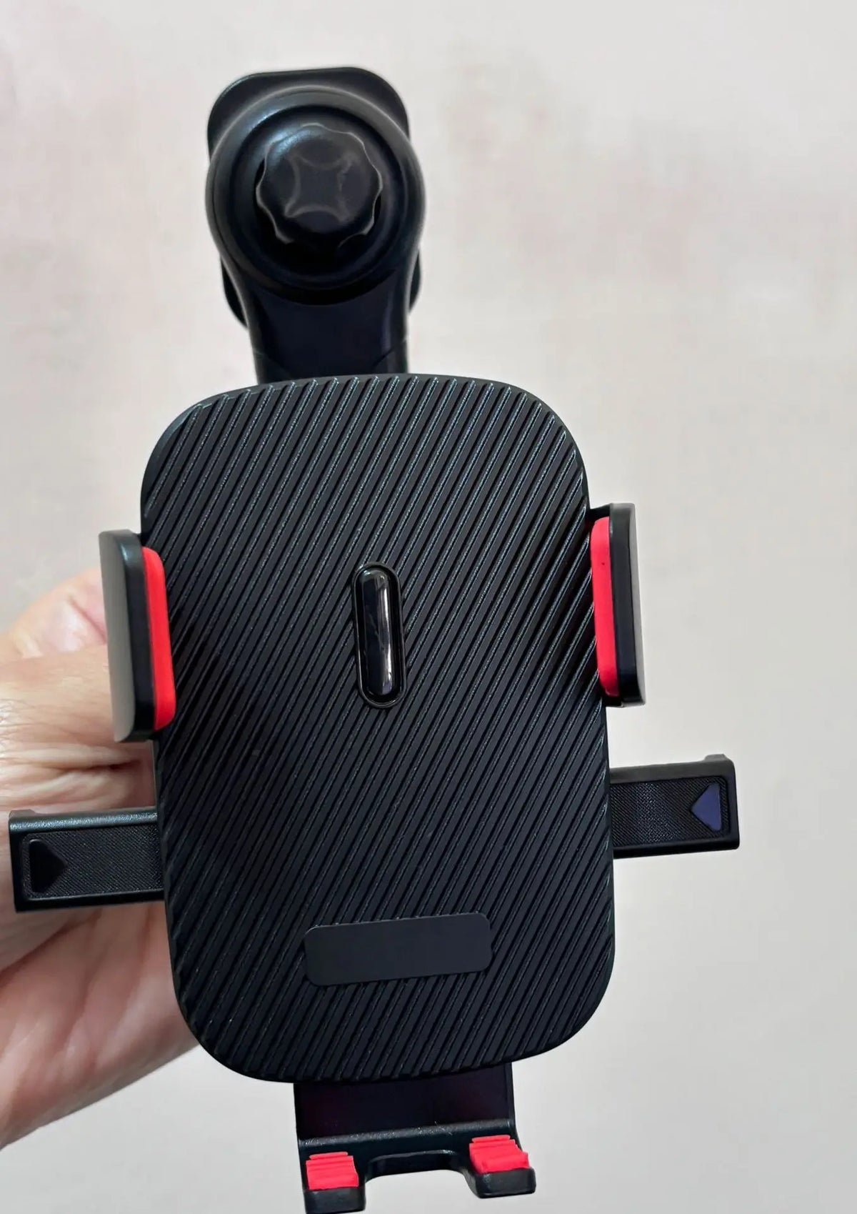 A black universal car phone mount with a gravity lock mechanism is held in a hand.