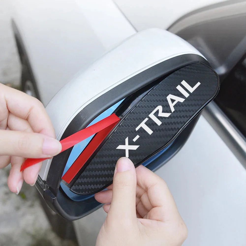 A hand is holding a black and white X-TRAIL car rain guard eyebrow cover for a rearview mirror.