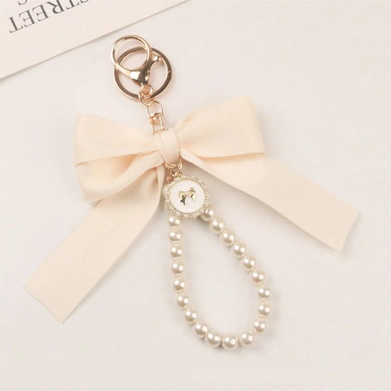 A delicate gold phone anti-loss lanyard featuring a round pearl bead pendant and a light pink bow.