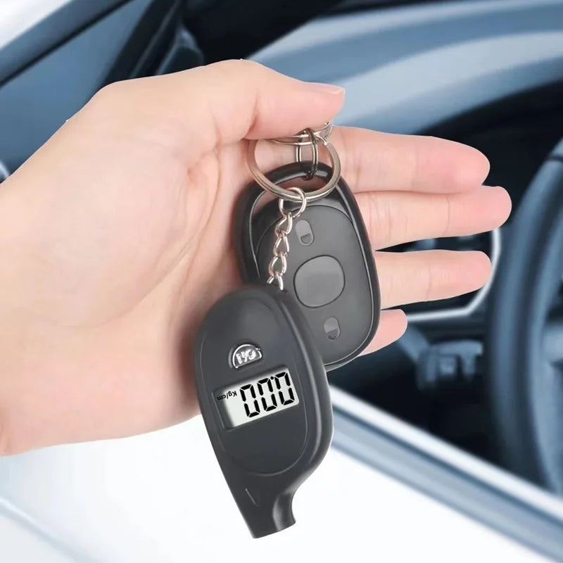 A hand holds a black digital tire pressure gauge with a metal keyring in a car interior setting.