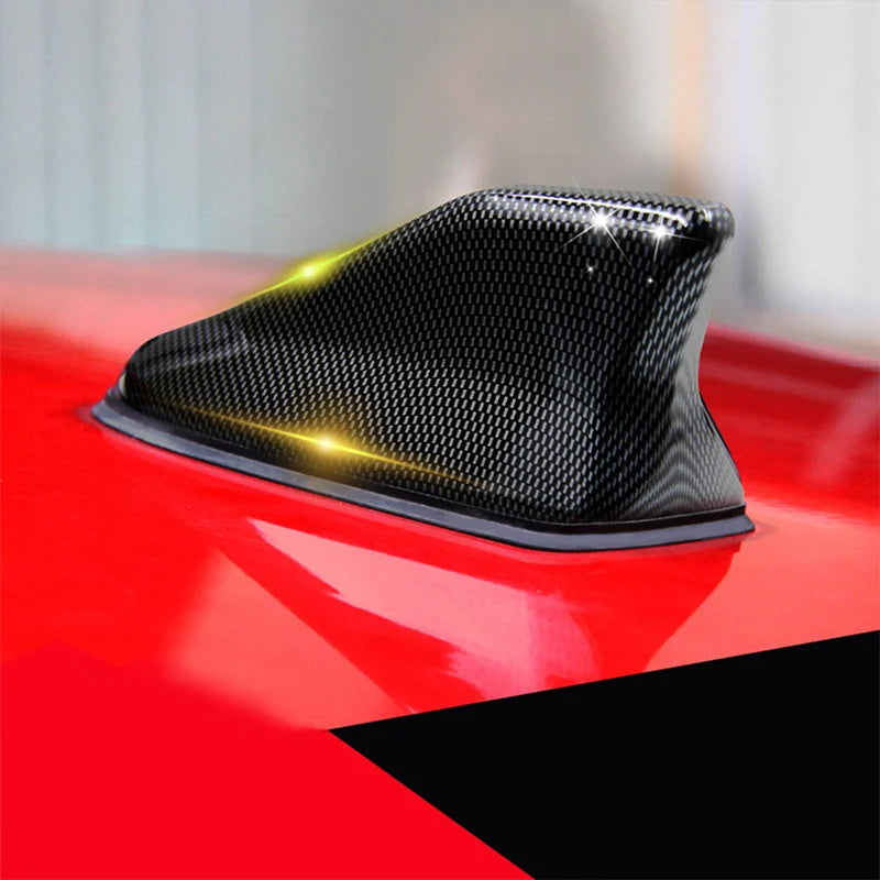 A black carbon fiber look roof mount antenna is shown mounted on a red surface.