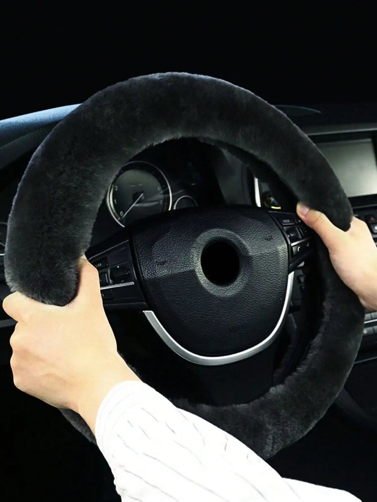 A hand grips a black winter plush steering wheel cover inside a car