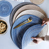 A stack of blue and beige woven placemats or coasters with a gold fork resting on the top one.