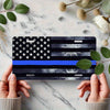 A hand holds a decorative aluminum flag sign featuring the American flag design and blue stripes on a marble surface.