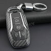A black carbon fiber style key fob cover with a metal chain, resting on a dark surface.