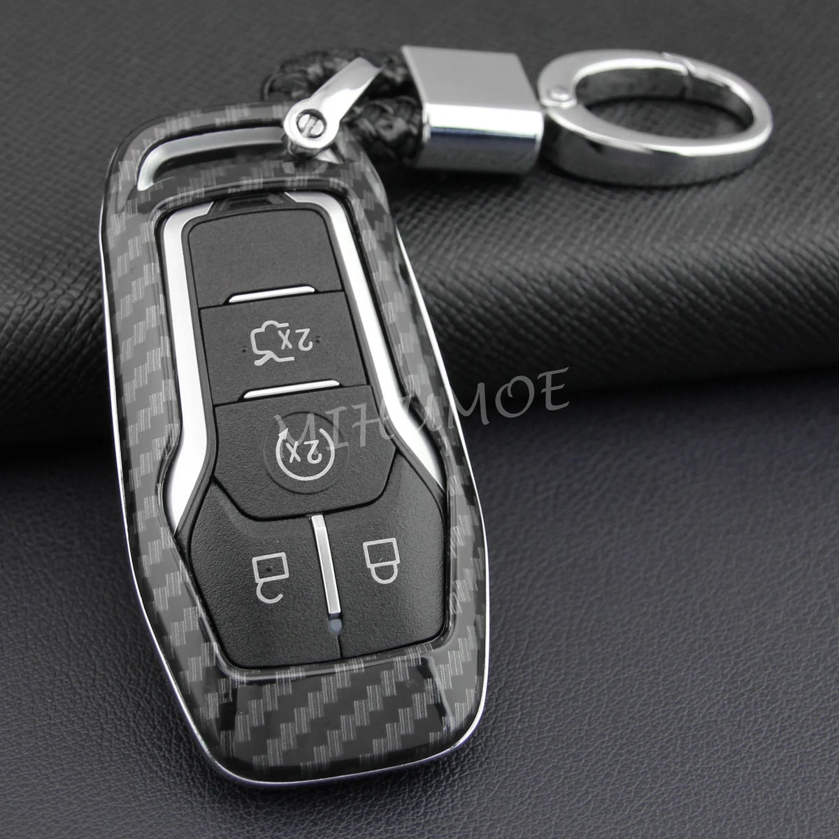 A black carbon fiber style key fob cover with a metal chain, resting on a dark surface.