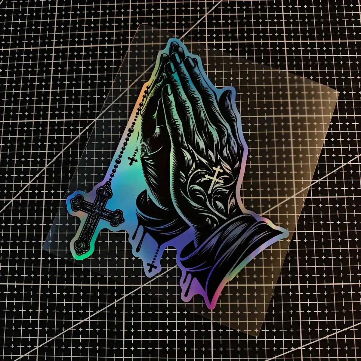 A dark decal of praying hands with a cross design, featuring iridescent blue and purple colors.