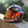 A glossy black full face motorcycle helmet with an orange visor featuring a fierce tiger eye design resting on a concrete led