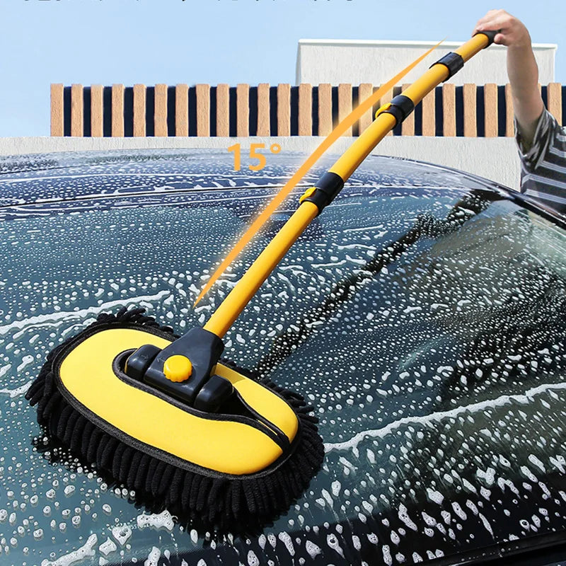 A yellow telescoping car wash mop is being used to clean water spots off a dark car's windshield.
