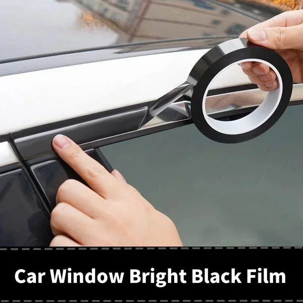 A hand is applying a roll of black window film to the trim of a car window.