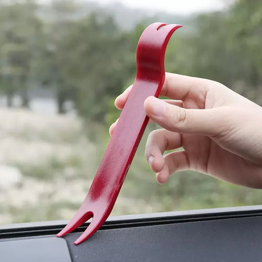 Una mano sostiene una herramienta de extracción de conectores eléctricos automotrices roja contra una superficie oscura.