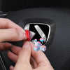 Hands are placing a 3D rhinestone Honda emblem decal onto a steering wheel.