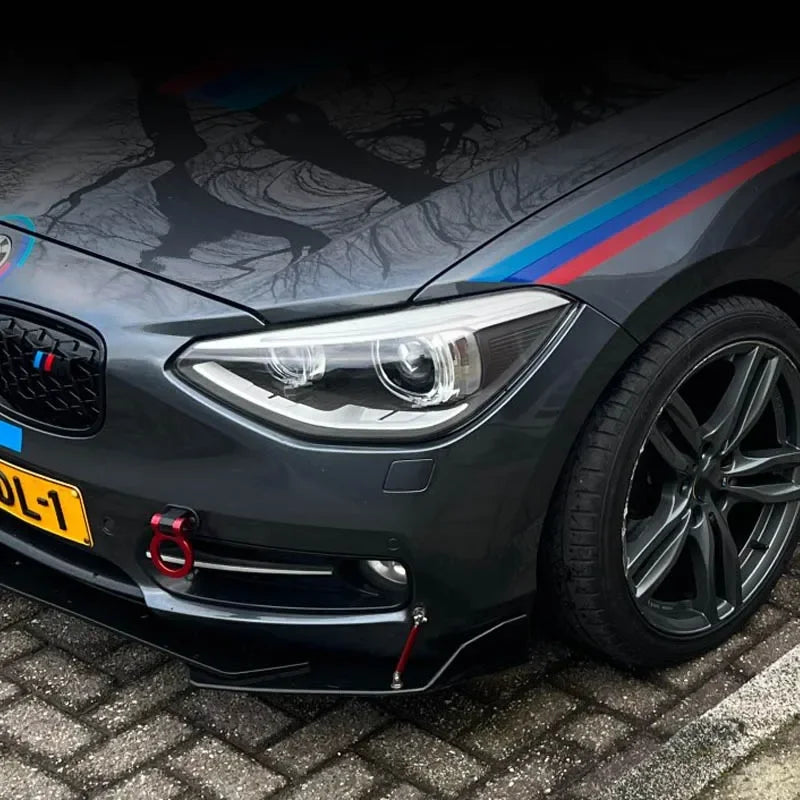 Close-up of a dark gray car with a blue and red stripe, showing the front headlight and grille area.