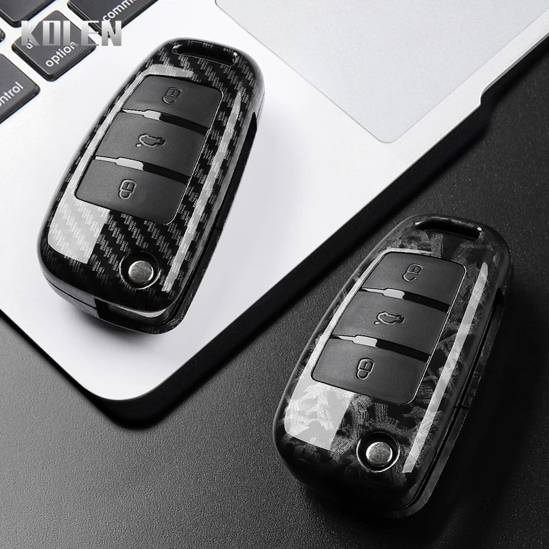 A close-up view of a black carbon fiber car key case cover resting on a laptop keyboard.