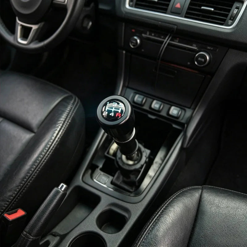 Close-up view of a black gear shift knob and console controls in a car interior.