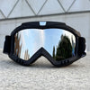 A pair of black windproof sports goggles with reflective lenses resting on a gray surface.