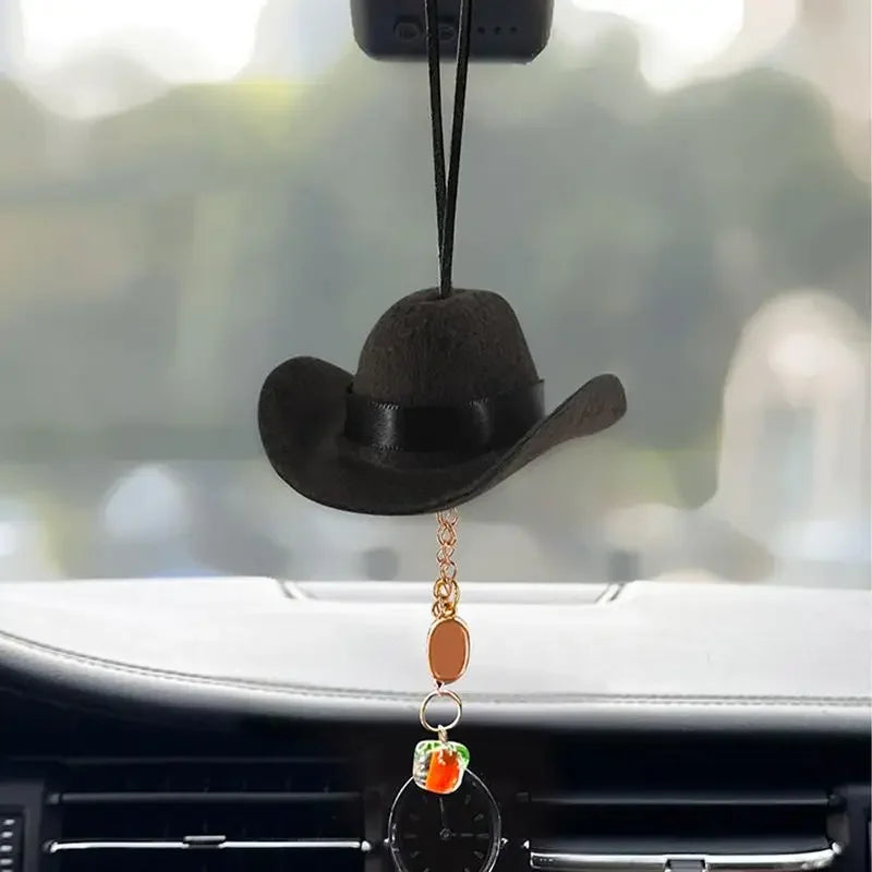 A black cowboy hat ornament with a gold chain hanging from it, displayed on a car interior.