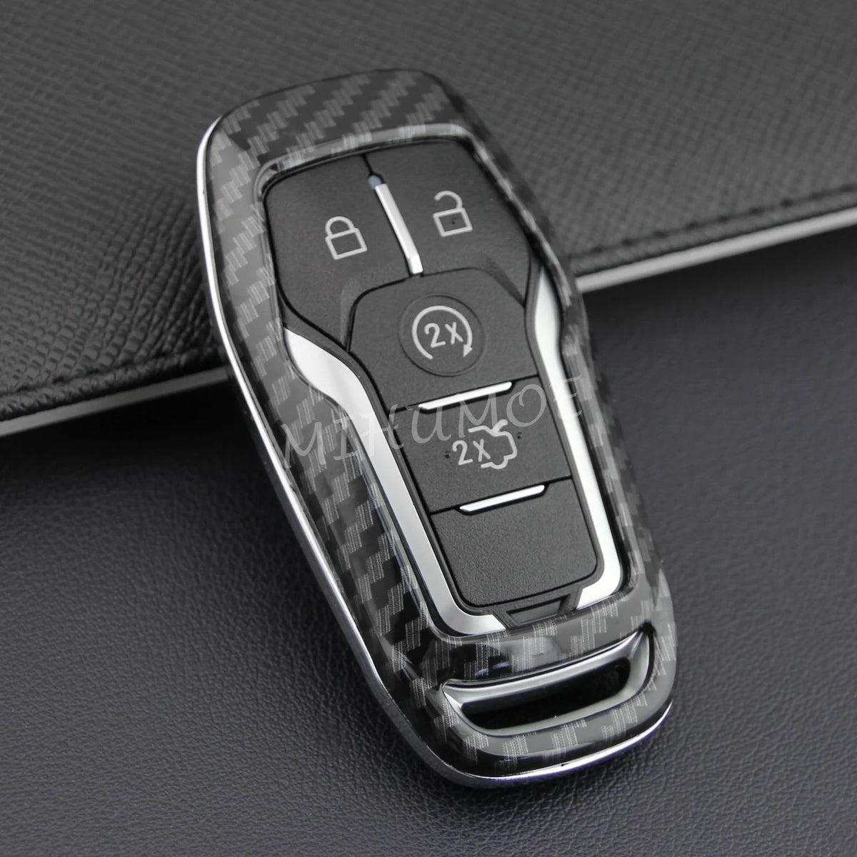 A black carbon fiber style key fob cover with a metal chain is shown against a dark background.